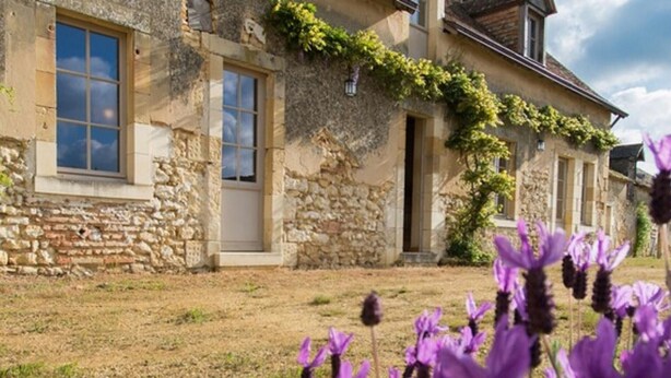 Un edificio de piedra con un jardín y flores moradas al frente.