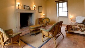 Una habitación acogedora con chimenea, muebles de mimbre, una cama y un ventanal grande.