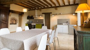 Un comedor con una mesa dispuesta para cuatro, una cocina al fondo y un techo de madera con vigas a la vista.