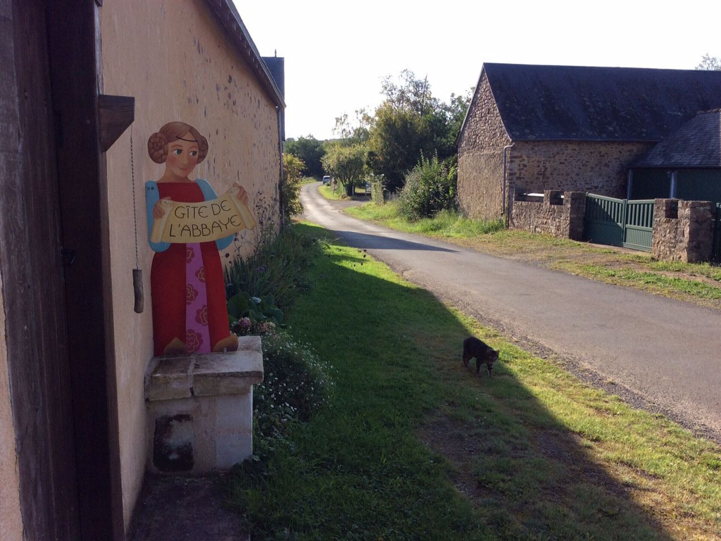 A rural road with a stone building on the left and a green gate on the right.