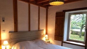 Une chambre à coucher avec une tête de lit en bois, une fenêtre donnant sur un paysage verdoyant et deux lampes de chevet.