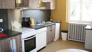 A compact kitchen with wooden cabinets, a built-in oven, a coffee maker, and a window providing natural light. - Spacieuse maison confortable avec jardin, à 20 min du centre-ville et proche du circuit des 24H du Mans (Le Mans)
