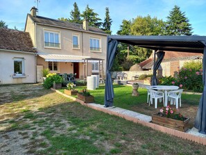 Una casa de dos pisos con un patio, mobiliario exterior y un jardín.