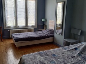 A bedroom with a bed, a chair, a radiator, a window with curtains, and a mirror. - Spacieuse maison confortable avec jardin, à 20 min du centre-ville et proche du circuit des 24H du Mans (Le Mans)