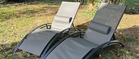Deux fauteuils de jardin, avec une structure en métal et un assise en tissu, sont placés sur une pelouse, avec des arbres en arrière-plan.