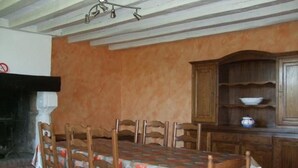 A dining area with a wooden table and chairs, a cabinet with shelves, and a fireplace. - Charming Cottage: 3BR, Cozy Fireplace, Large Garden, Near Bercé Forest (Saint-Mars-d'Outillé)