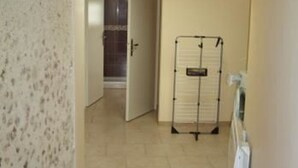 A hallway with a tiled floor, a door leading to a bathroom, and a drying rack against the wall. - Charming Cottage: 3BR, Cozy Fireplace, Large Garden, Near Bercé Forest (Saint-Mars-d'Outillé)