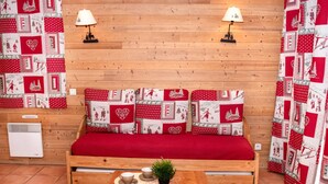 A cozy room with a wooden sofa, two wall-mounted lamps, a small table with cups and a plant, and a patterned curtain. - Studio for 4 with balcony and parking in Pra Loup 1500 (Uvernet-Fours)