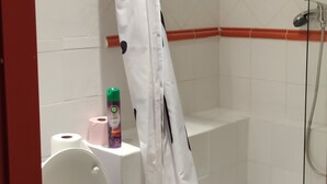 Ein Badezimmer mit Dusche, Toilette und Ablagefläche mit Lufterfrischer und Toilettenpapier.