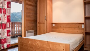 Ein Zimmer mit Holzboden, einem Bett, einem Fenster und einer Tür, die auf einen Balkon führt.