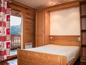 Una habitació de fusta amb un llit, una finestra i una porta que dona a un balcó.