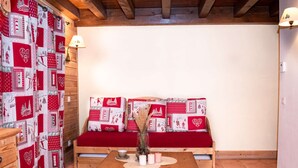 Ein gemütliches Zimmer mit einer hölzernen Bank, einem kleinen Tisch und einem gemusterten Vorhang.
