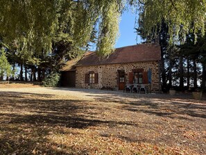 Um edifício de pedra com telhado em tijolos, rodeado por árvores e um caminho de cascalho.