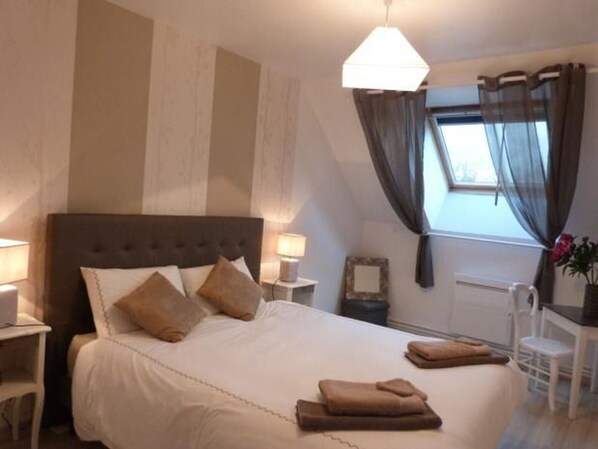 A neatly made bed with pillows, a bedside table with a lamp, a chair, and a window with curtains. - Renovated farmhouse with terrace, internet, and garage near Vallon-sur-Gée (Vallon-sur-Gée)