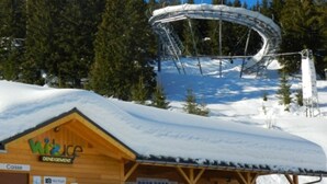A wooden lodge with a snow-covered roof, a ski lift in the background, and a sign that reads "Wikure Dinegeiment."