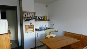 A compact kitchen with a refrigerator, a sink, and a wooden dining table.
