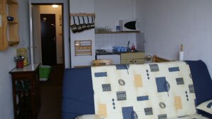 A small, compact living space with a kitchenette, a bed with a patterned blanket, and a ceiling fan.