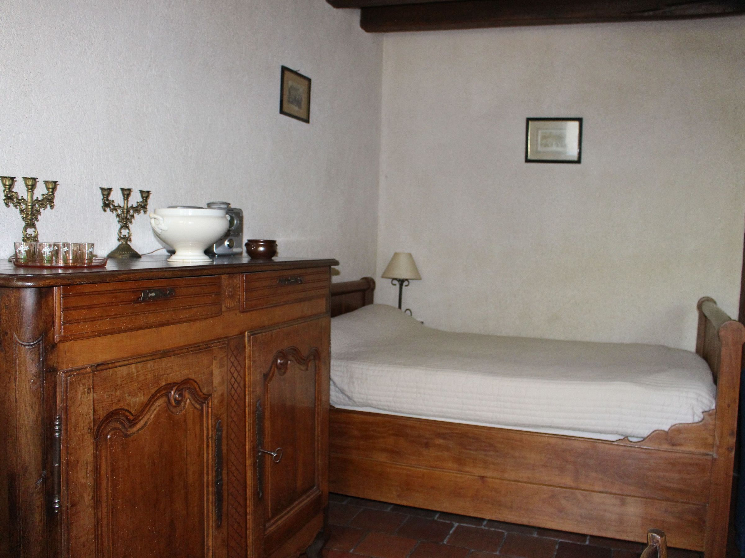 Een kamer met een houten bed, een dressoir met lades, een lamp en twee prenten aan de muur.