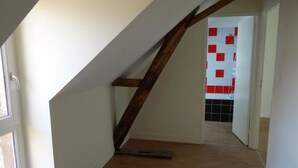 Um corredor estreito com vigas de madeira, soalho em azulejos e uma porta que dá para um espaço com azulejos vermelhos e brancos.