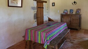 Una habitación con un banco de madera, una mesa con mantel a rayas, un mueble de madera y un cuadro enmarcado en la pared.