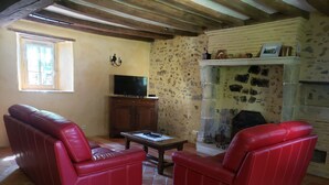 Una sala de estar con chimenea de piedra, sofás de cuero rojo, un televisor sobre un mueble de madera y suelo de baldosas.