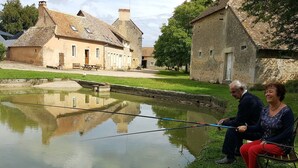 Un couple est assis au bord d’un canal paisible, avec en arrière-plan des bâtiments traditionnels en pierre.