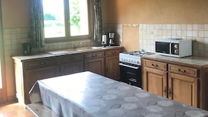 Une cuisine avec des meubles de rangement en bois, une cuisinière à gaz, un four à micro-ondes et une fenêtre avec des rideaux.