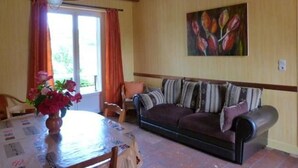 Een gezellige woonkamer met een houten plafond, een bank met gestreepte kussens, een tafel met een bloevas en een schilderij van bloemen aan de muur.