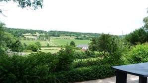 Een terras met een tafel en stoelen, omgeven door weelderige begroeiing en een uitzicht op het landschap.