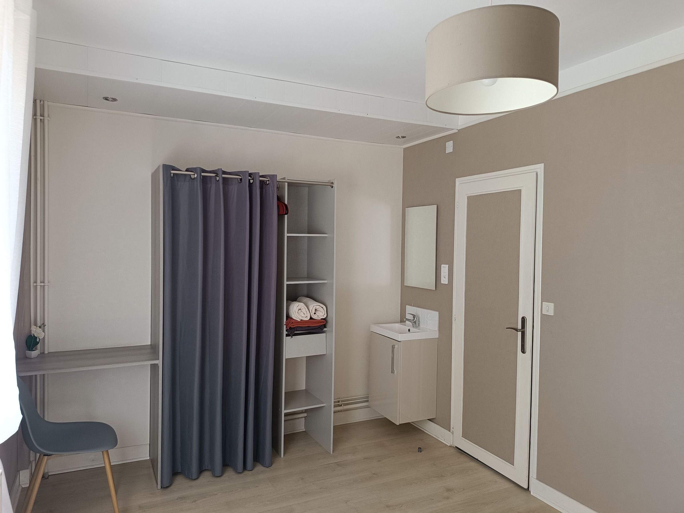 Een kamer met een bureau, een stoel, een kledingkast, een spiegel en een wastafel.