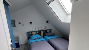 Quarto com duas camas, teto inclinado e claraboia.