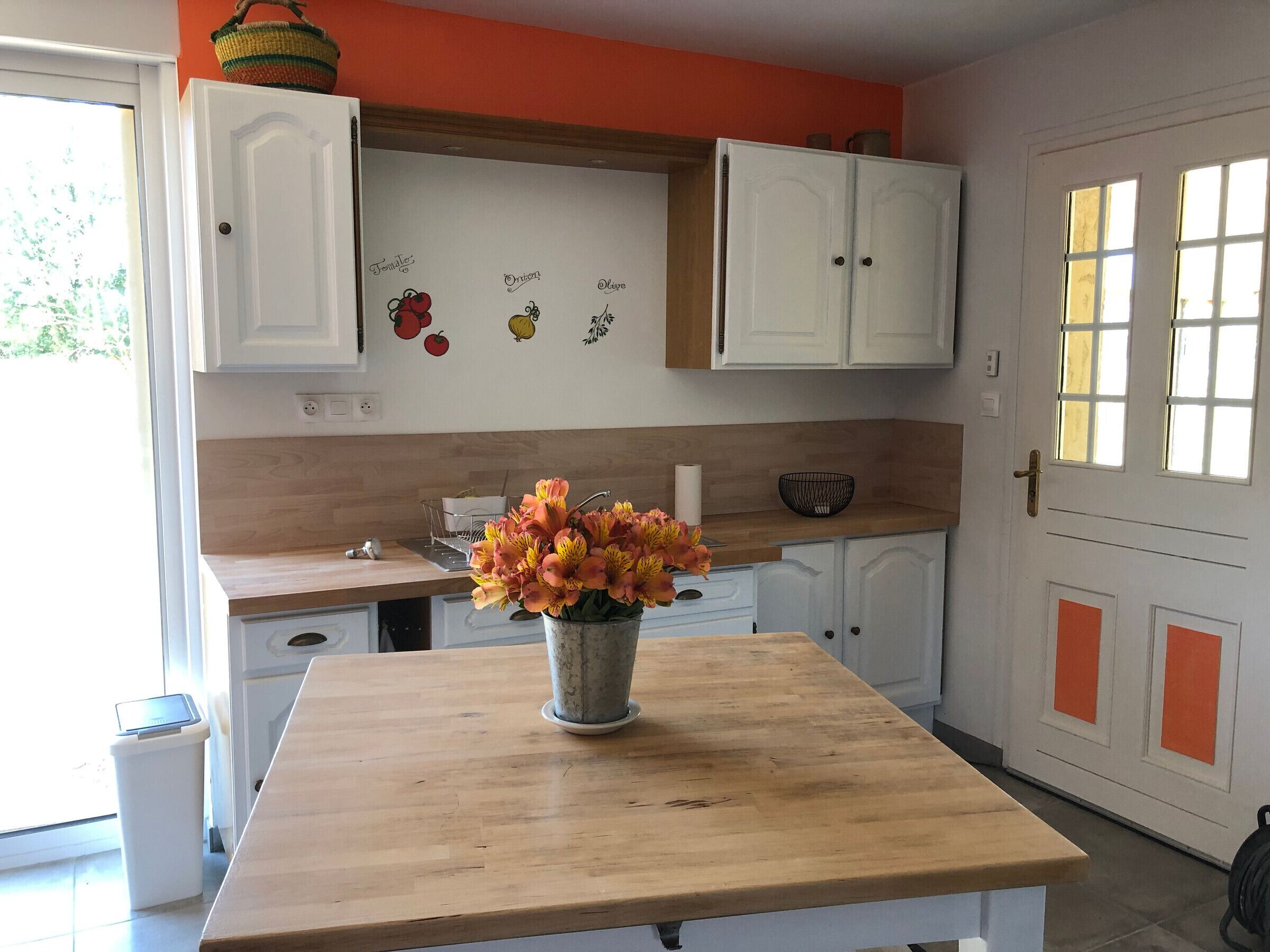 Een keuken met witte kastjes, een houten aanrechtblad en een vaas met bloemen op een tafel.