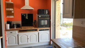 Uma cozinha compacta com armários brancos, forno preto, micro-ondas e cafeteira.