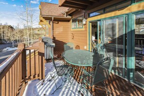 A wooden deck with a grill, metal chairs, and a table.