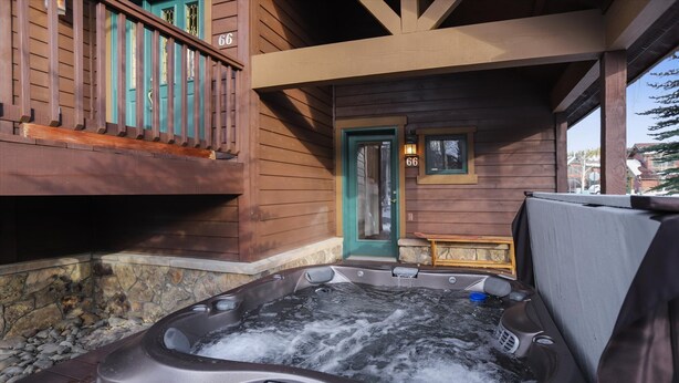 A hot tub outside a wooden cabin with a stone wall and a door marked with the number 66.