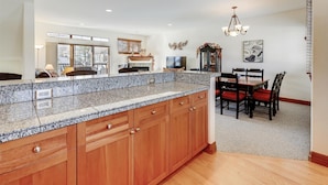 A kitchen with granite countertops, wooden cabinets, a dining area with a table and chairs, and a chandelier.