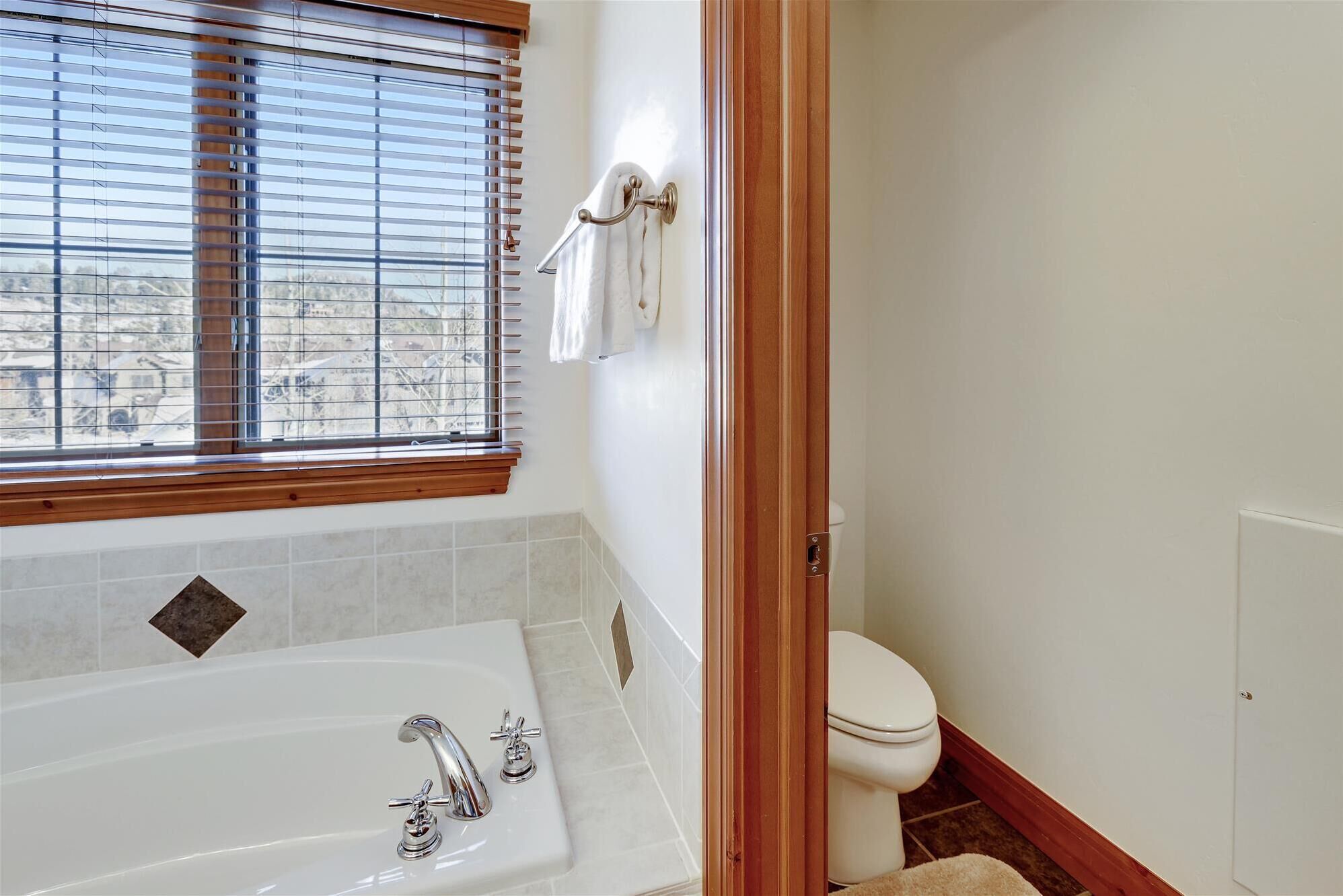 Un baño con bañera, inodoro y ventana con persianas.