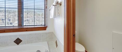 Un baño con bañera, inodoro y ventana con persianas.