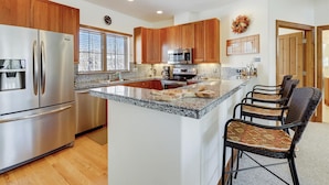 A modern kitchen with wooden cabinets, stainless steel appliances, a granite countertop, and a bar area with wicker chairs.