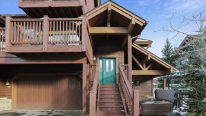 A multi-level wooden building with a green door, a staircase, and a hot tub in the yard.