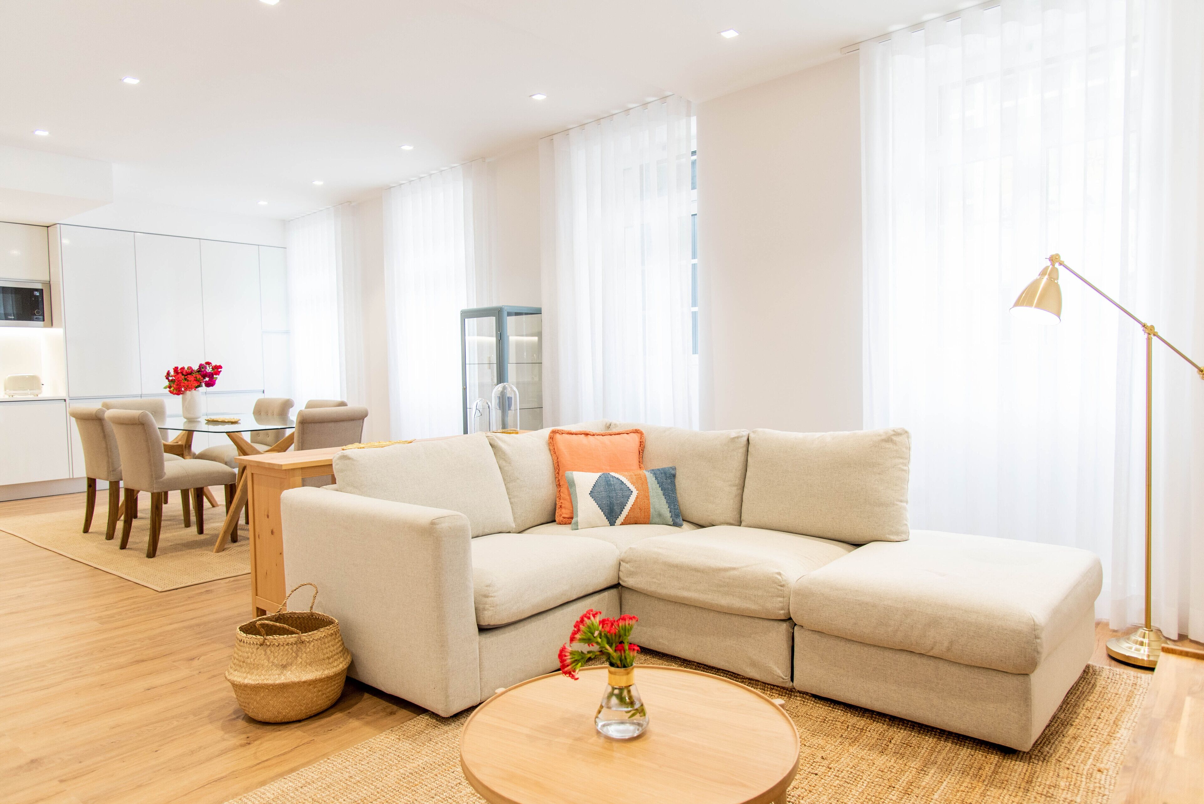 A modern living room with a beige sectional sofa, a round wooden coffee table, and a dining area with a glass table and chairs.