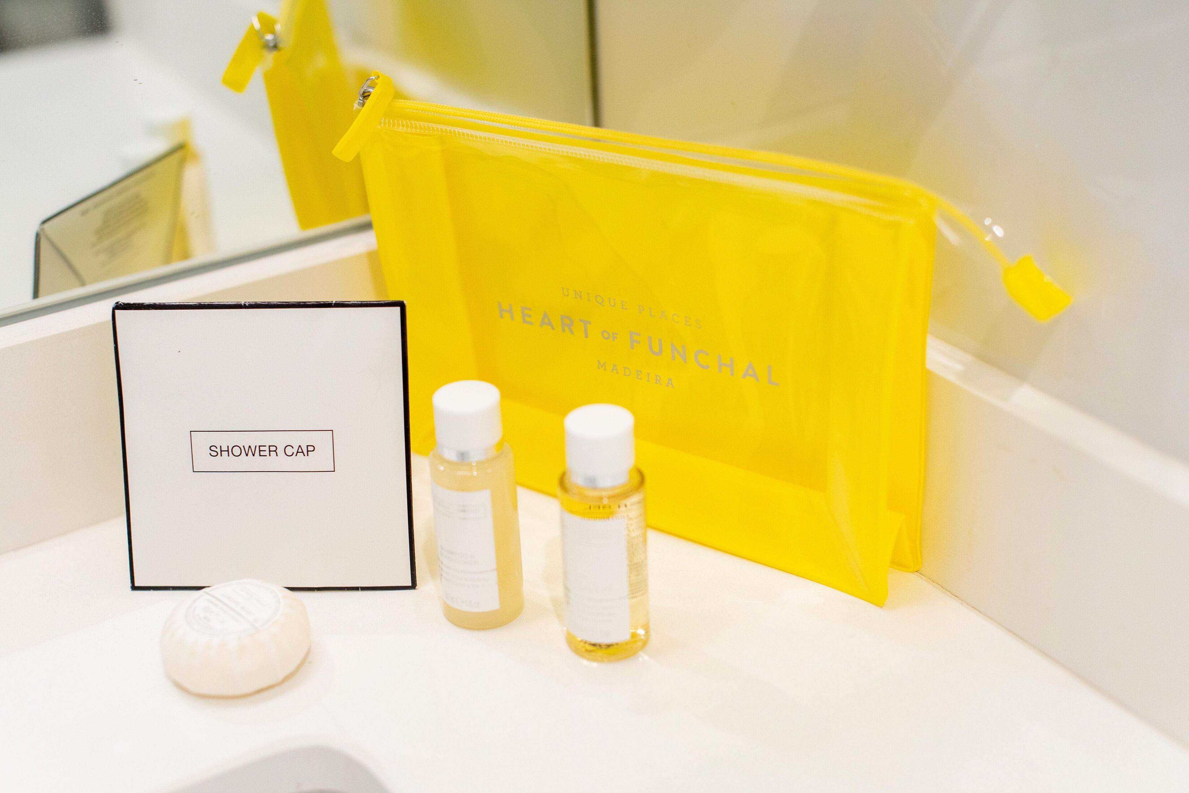 A bathroom vanity with a shower cap, two bottles of liquid, and a yellow bag.