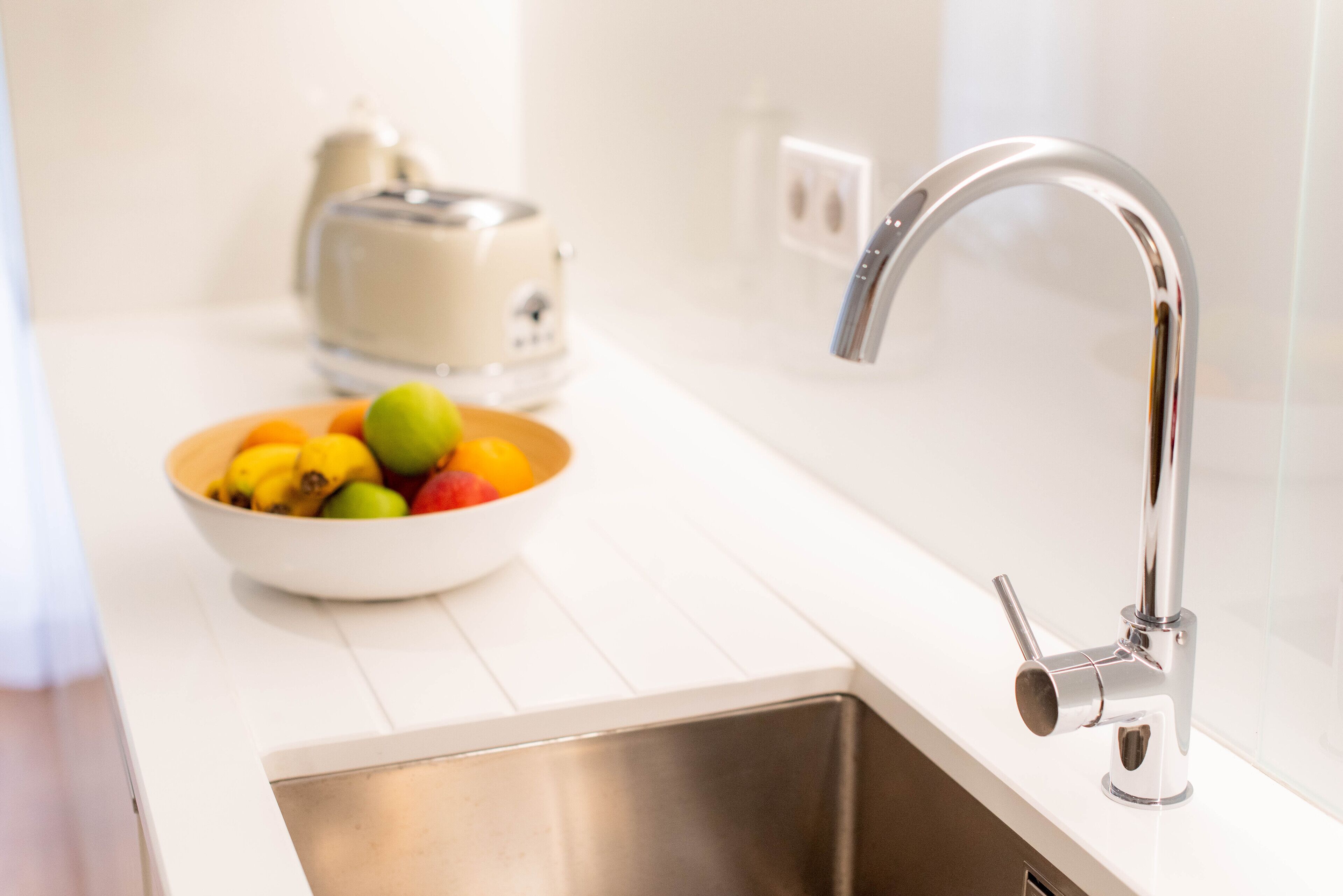 A kitchen with a stainless steel sink, a bowl of fruit, and a toaster.