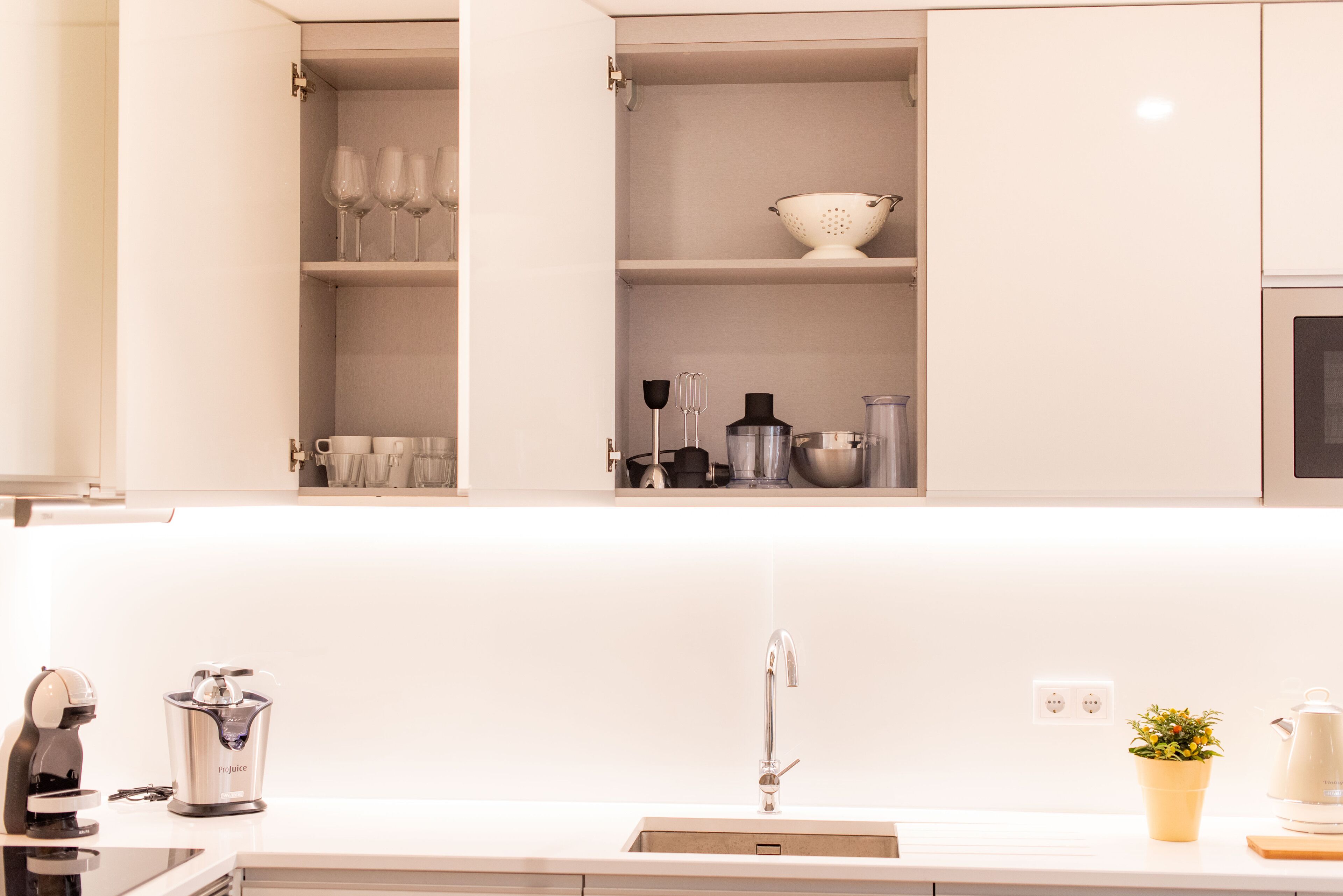 A modern kitchen with white cabinets, a stainless steel sink, and various kitchen appliances.