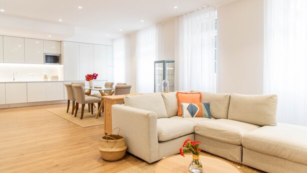 A modern living room with a beige sofa, a round coffee table with a vase of flowers, and a dining area with a table and chairs. - Apartamentos Fernão Ornelas (Funchal)