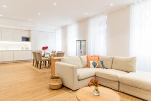 A modern living room with a beige sofa, a round coffee table with a vase of flowers, and a dining area with a table and chairs. - Apartamentos Fernão Ornelas (Funchal)