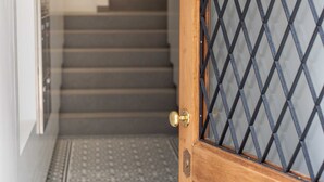A wooden door with a diamond-patterned glass panel, leading to a staircase with a patterned floor. - Apartamentos Fernão Ornelas (Funchal)