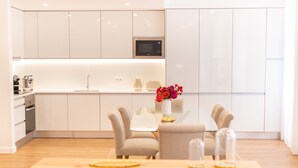 A modern kitchen with white cabinets, a microwave, and a dining area with a table and chairs. - Apartamentos Fernão Ornelas (Funchal)