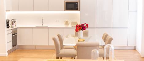 Una cocina moderna con armarios blancos, un microondas y una zona de comedor con mesa y sillas.