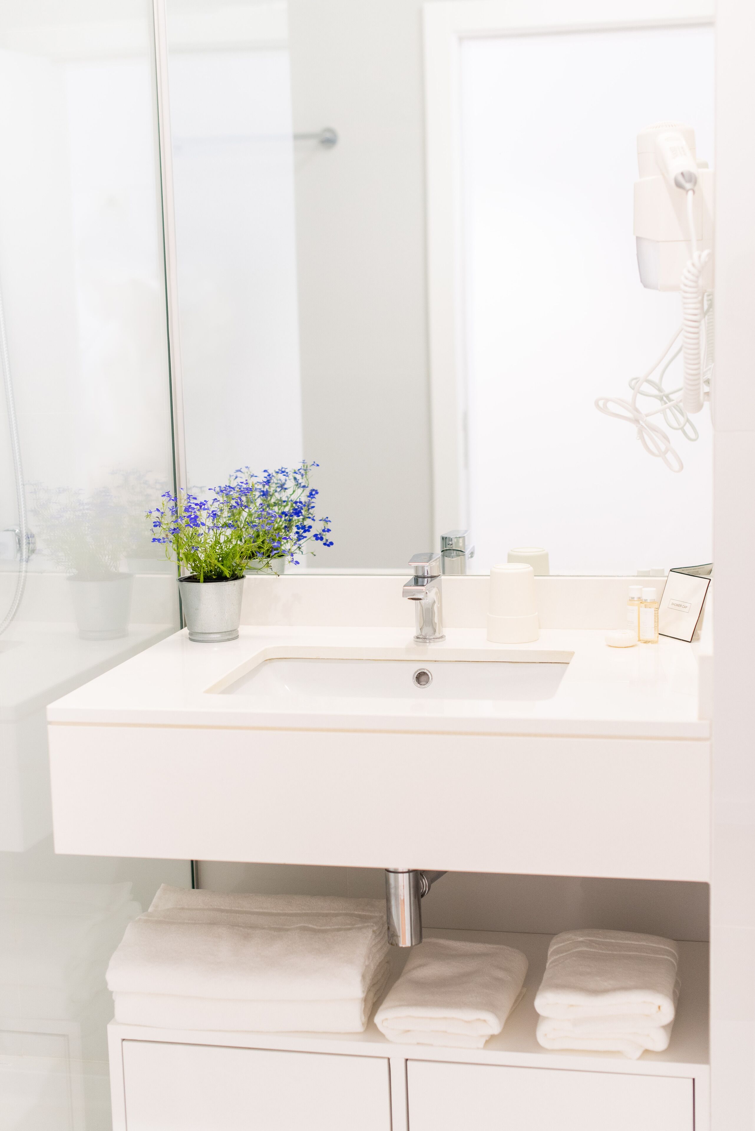 A bathroom with a white sink, a mirror, a hairdryer, and towels.